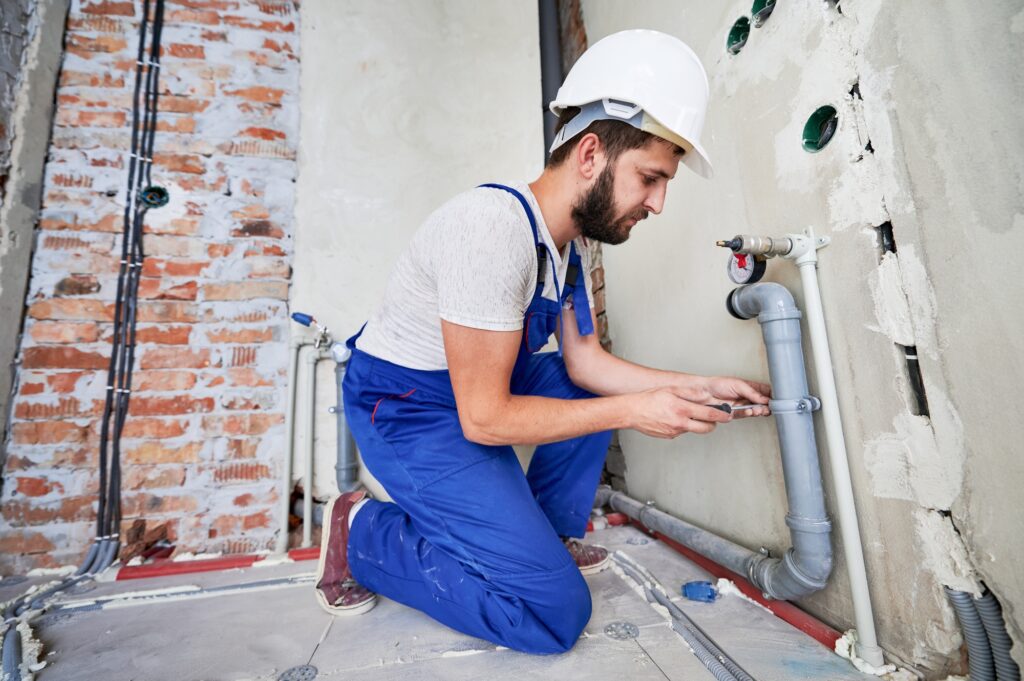 Young plumber working with grey sewer pipes, fixing them to wall