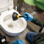 Cleaning toilet stuck with suction cup. Hands in gloves holding ventuz in toilet.