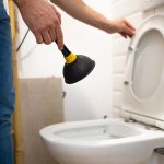 Serviceman repairing toilet with hand plunger. Clogged toilet.
