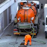 Worker lowers sewer hose into sewer pit.